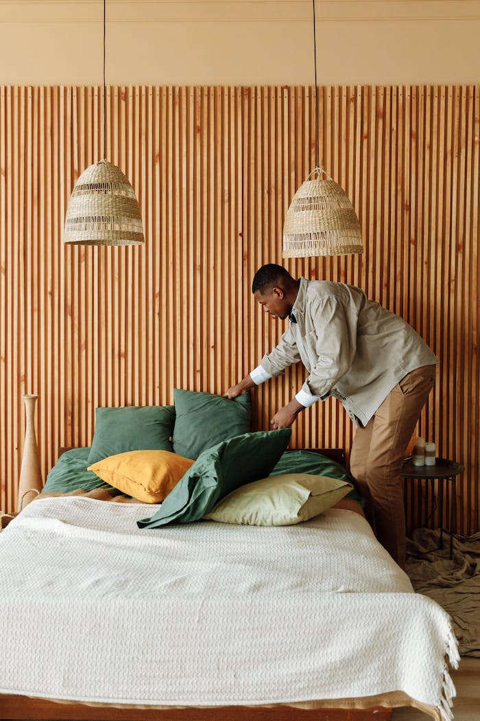 Man arranging pillows in modern bedroom with wooden decor.